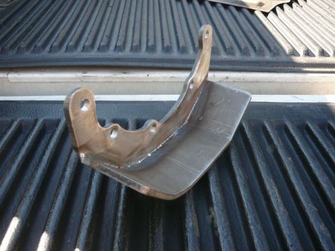 1988 Ford Bronco - A close-up view of a metal bracket with multiple mounting holes, placed in the ribbed bed of a pickup truck.