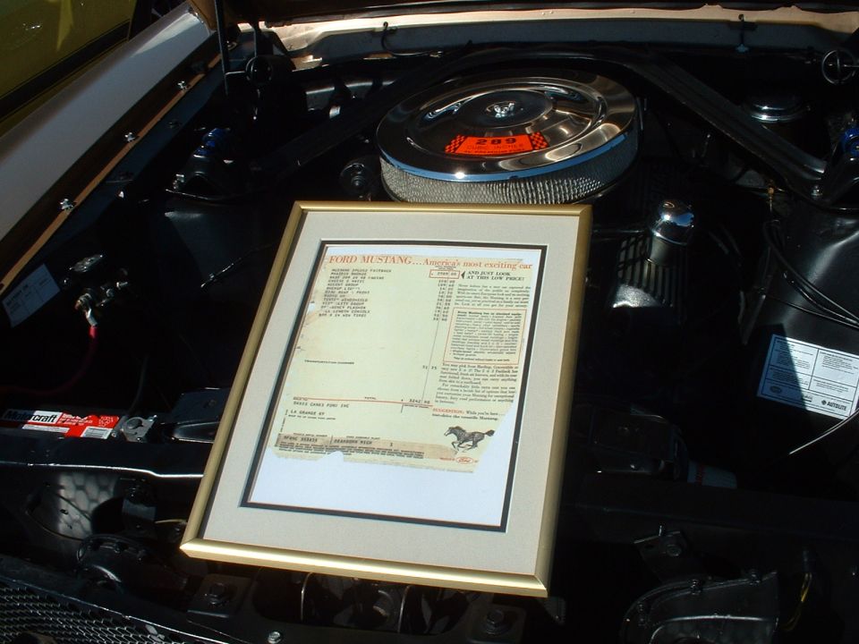 Framed window sticker for a Ford Mustang sits on top of an engine bay