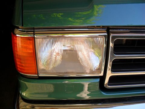 1990 Ford Bronco - Close-up of the front corner of a green 1990 Ford Bronco, showing the headlight and part of the chrome grille.