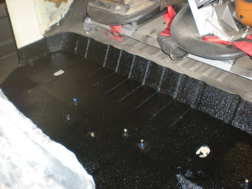Black textured vehicle floor with visible seat mounts and red seatbelt straps