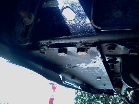 1989 Ford Bronco - Underside view of vehicle frame components, showing bolted connections and metal plates.
