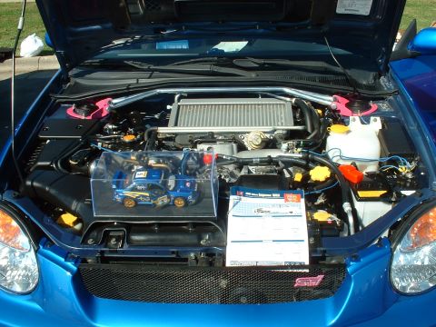 1995 Ford Crown Victoria - Engine bay of a blue Subaru WRX STI, an intercooler and a display with a model car and information sheet.