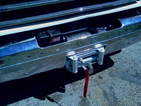 1989 Ford Bronco - A winch is mounted to a chrome bumper with a red strap hanging from the hook.