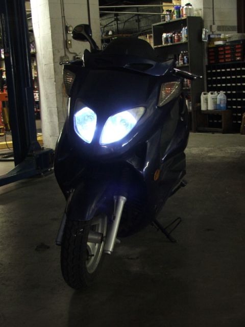 2008 Yamaha Zuma - A dark blue scooter is parked in a garage with its headlights on.
