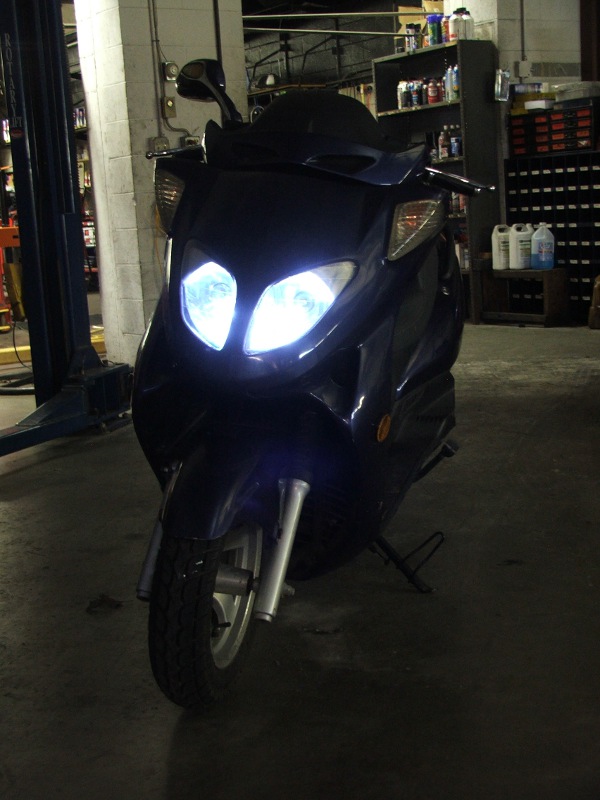 Dark blue scooter with bright headlights, parked indoors