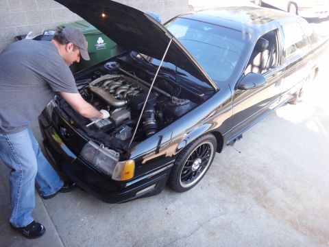 1993 Ford Taurus - Mechanic inspects the engine bay of a black 1993 Ford Taurus sedan.