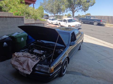 1993 Ford Taurus - A black sedan with its hood open is parked on a driveway, with other vehicles in the background.