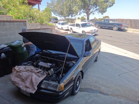 1993 Ford Taurus - Mechanic working on a black 1993 Ford Taurus sedan with its hood open.