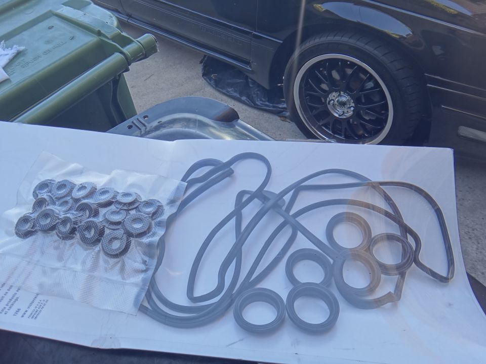 Gasket set laid out on paper with a car wheel and green trash bin in background