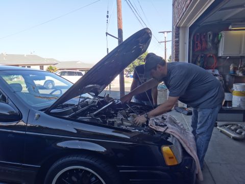 1993 Ford Taurus - Two men are working on the engine of a 1993 Ford Taurus with the hood up.