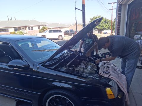 1993 Ford Taurus - Men work on the engine of a black sedan, which appears to be a 1991 model based on its body style.