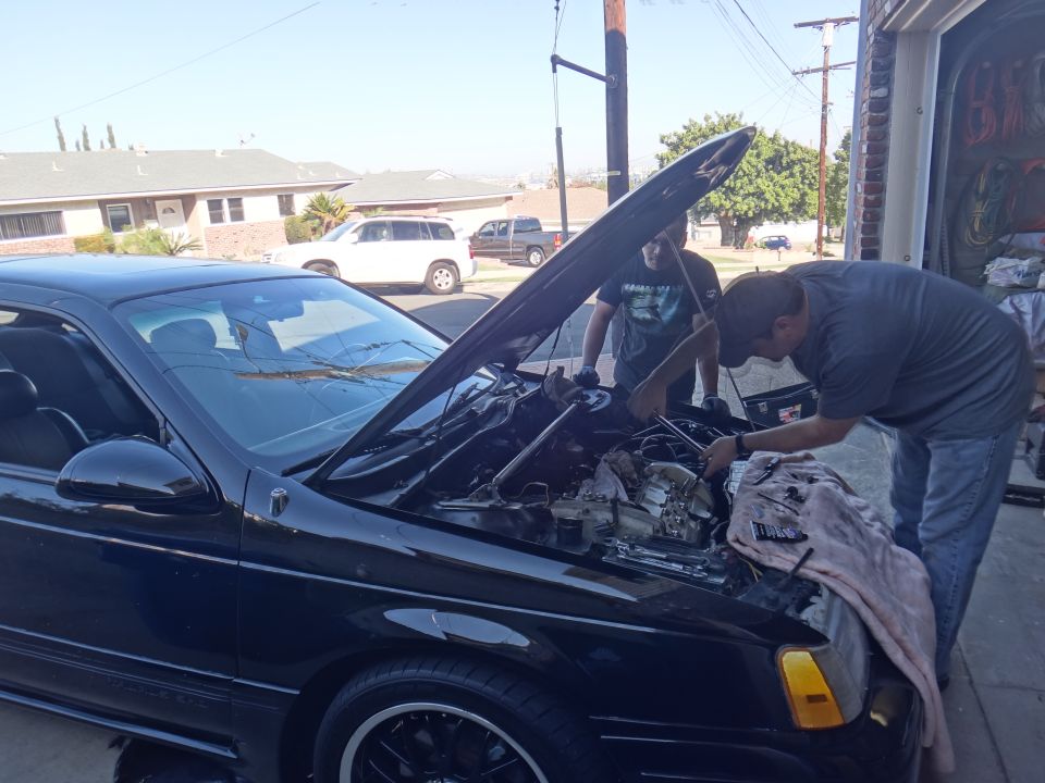 Black sedan with hood open, men working on engine. Front quarter view