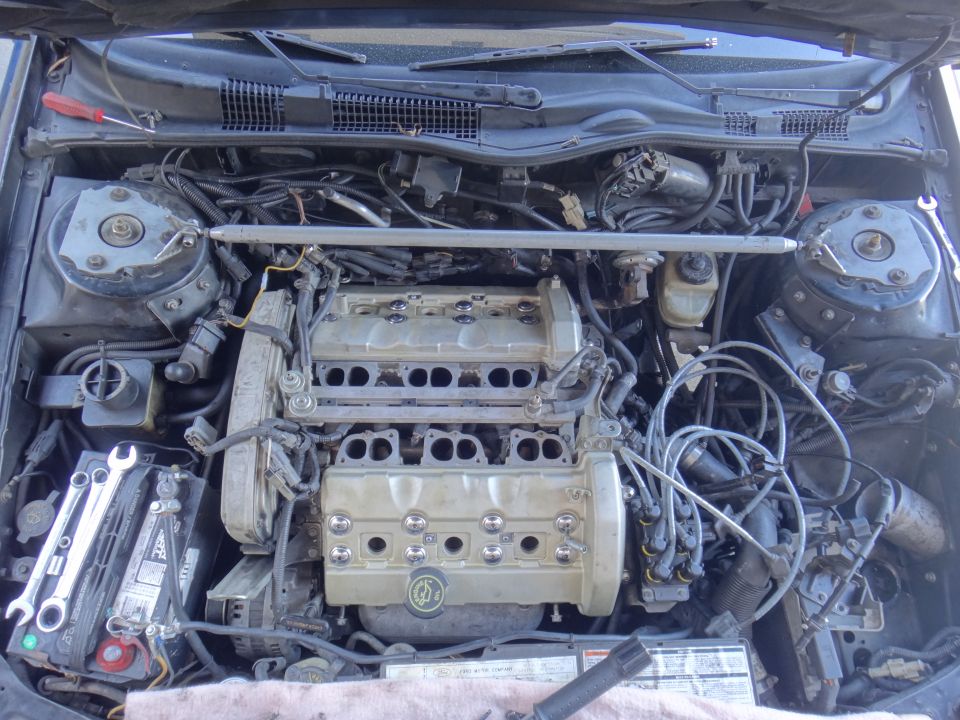 Engine bay with V6 engine, tools on battery, and wiring