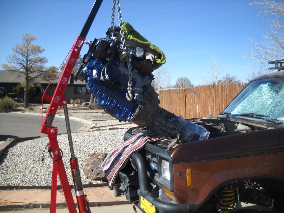 Brown SUV with engine being removed by a red engine hoist