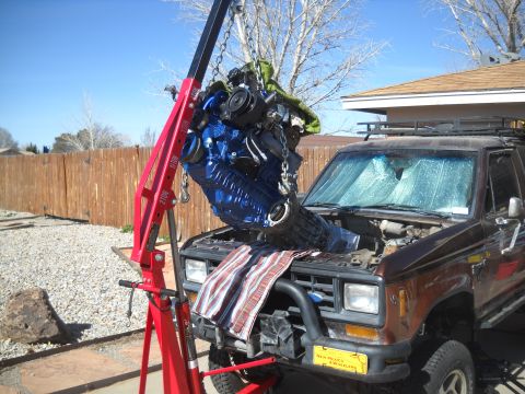 1992 Ford Explorer - An engine is being removed from a brown SUV using a red engine hoist. The Supermotors.net logo is visible on the bumper.