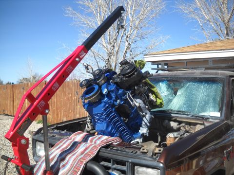 1992 Ford Explorer - Engine hoist lifting a blue engine out of a vehicle with a cracked windshield.
