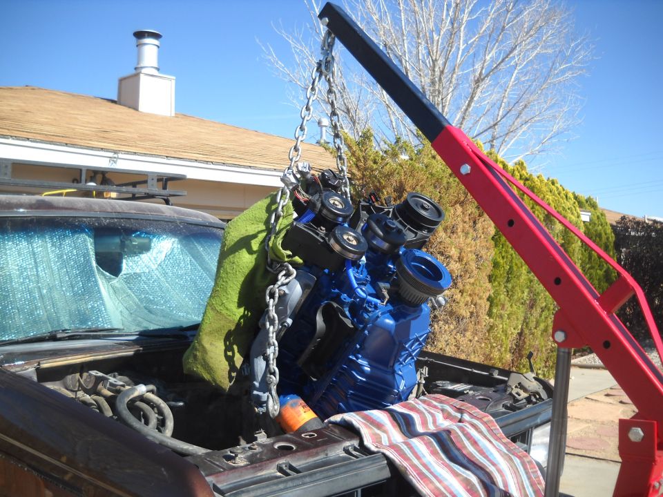 Engine being lifted by a red engine hoist out of an open hood. A green blanket is draped over part of the engine
