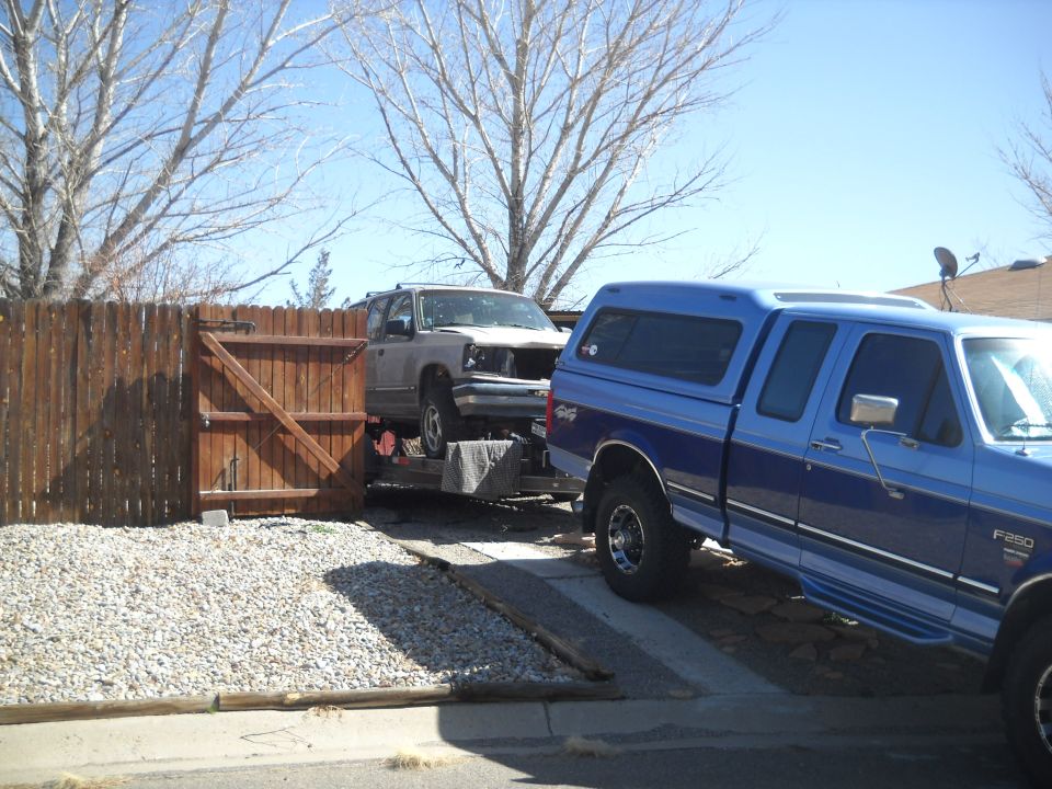 Gray SUV on trailer, front bumper missing, towed by blue pickup truck