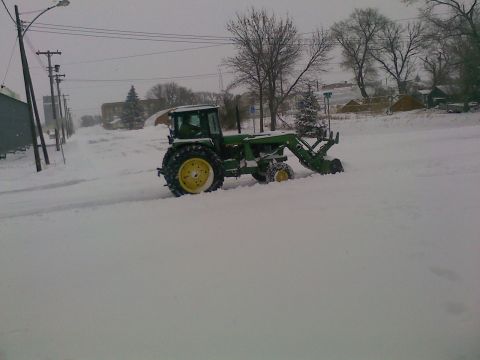 1966 Ford Bronco - A green tractor with yellow wheels is clearing snow from a street during a blizzard.
