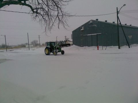 1966 Ford Bronco - A green tractor with a front loader is parked in a snowy area next to a large building.