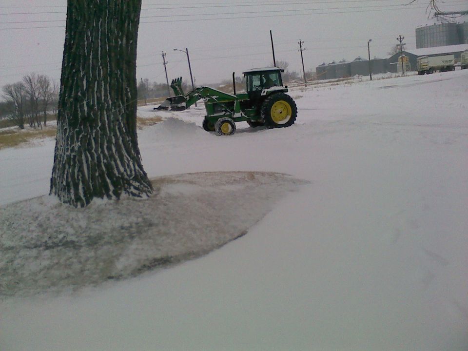 Tractor with front loader in a snowy field next to a large tree