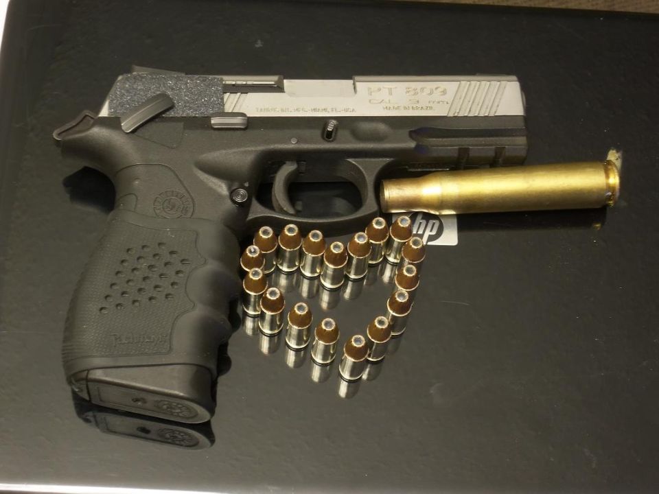Semi-automatic pistol with magazine removed, surrounded by cartridges, with a large caliber round next to it