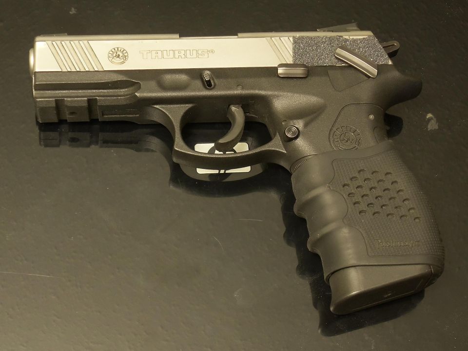 Black and silver Taurus pistol with textured grip and magazine visible on a dark reflective surface