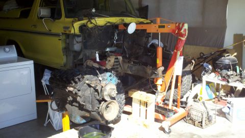 1978 Ford Bronco - A yellow 1978 Ford Bronco is undergoing engine removal with an engine hoist, with a washing machine nearby.