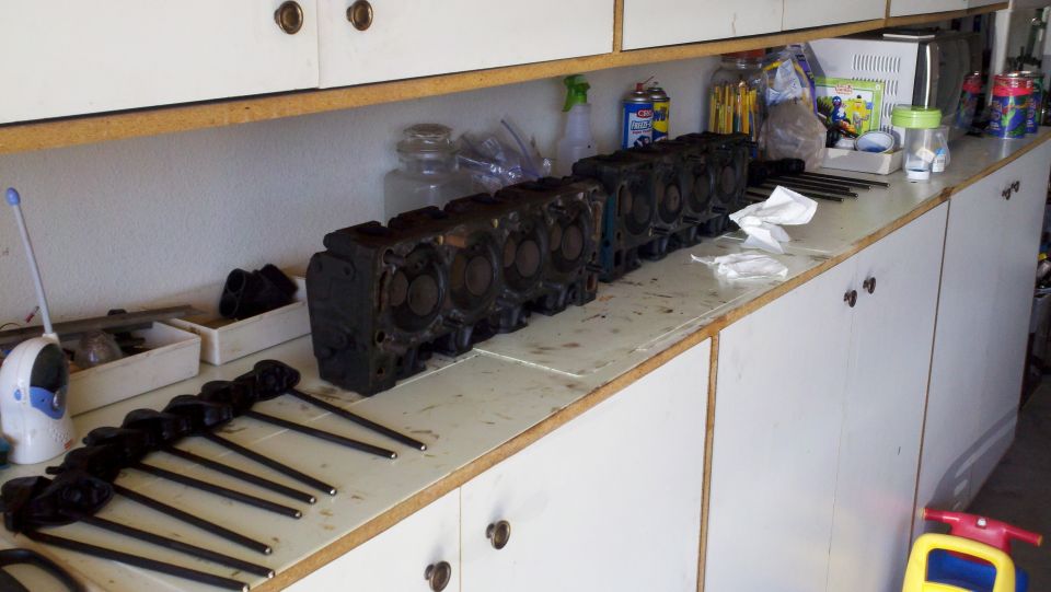 Several engine cylinder heads lined up on a workbench, with a set of pushrods in front