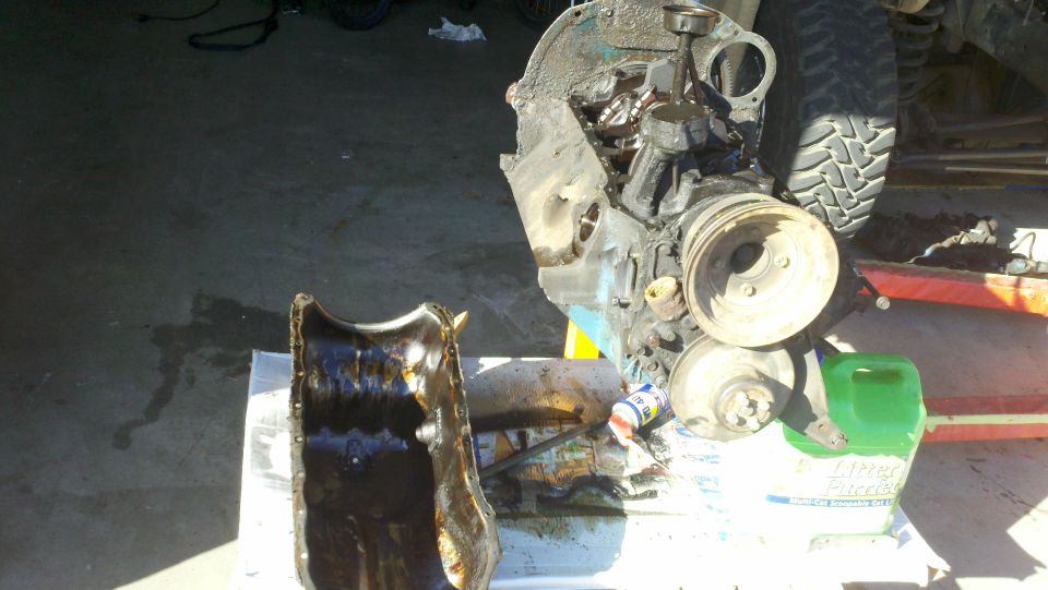 Disassembled engine block and oil pan with various tools and fluids nearby