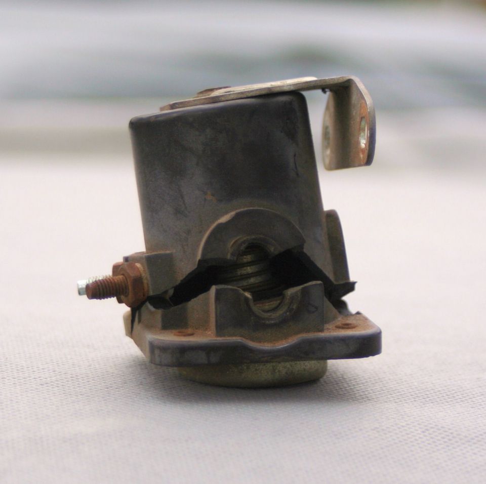 Cracked black plastic battery component with metal bracket and rusty bolt