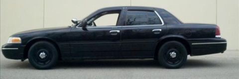 2004 Ford Crown Victoria - Side profile of a black 2004 Ford Crown Victoria sedan parked against a light-colored wall.