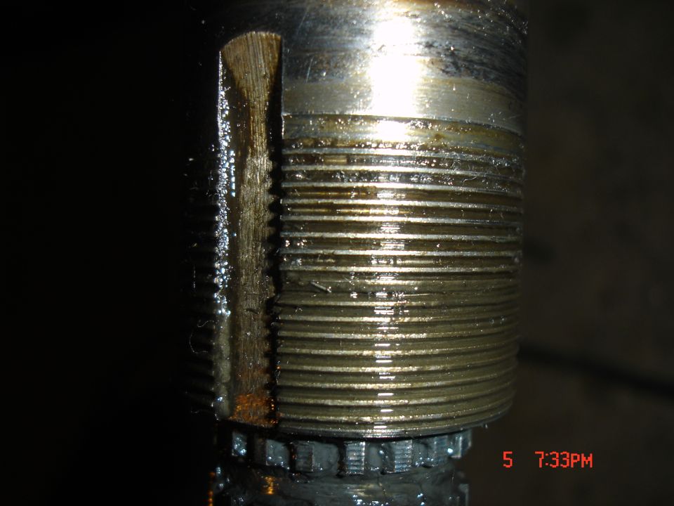 Close-up of a threaded metal shaft with oil and some wear