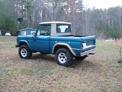 1969 Ford Bronco - This blue Ford Bronco is seen from the rear quarter angle, parked outdoors in a wooded area.