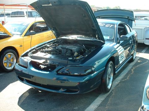 1995 Ford Crown Victoria - A dark teal 1995 Ford Mustang GT is displayed with its hood open, revealing the engine, next to a yellow Mustang.