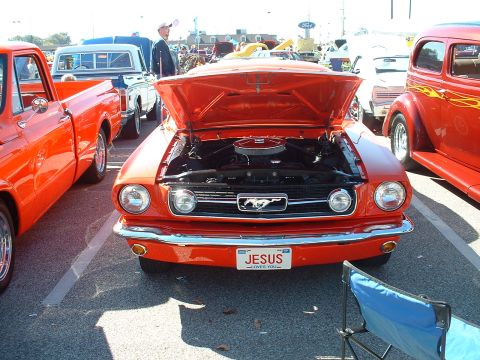 1995 Ford Crown Victoria - A classic orange Ford Mustang is displayed with its hood open, the engine bay at an outdoor car show.