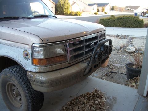 1996 Ford Bronco - A dirty Ford truck sits parked in a driveway, its front end covered in mud and debris.