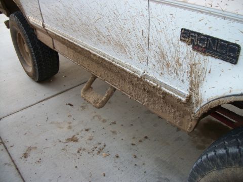 1996 Ford Bronco - Mud splatters cover the side of a white 1996 Ford Bronco, obscuring the paintwork and running boards.