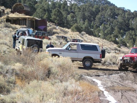 1996 Ford Bronco - A group of off-road vehicles navigate a muddy path near an old mining structure on a hillside.