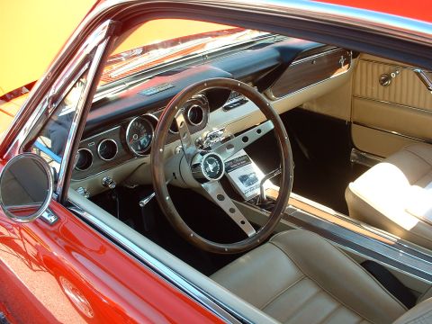 1995 Ford Crown Victoria - The interior of a classic red 1965 Ford Mustang features a wood-rimmed steering wheel and tan upholstery.