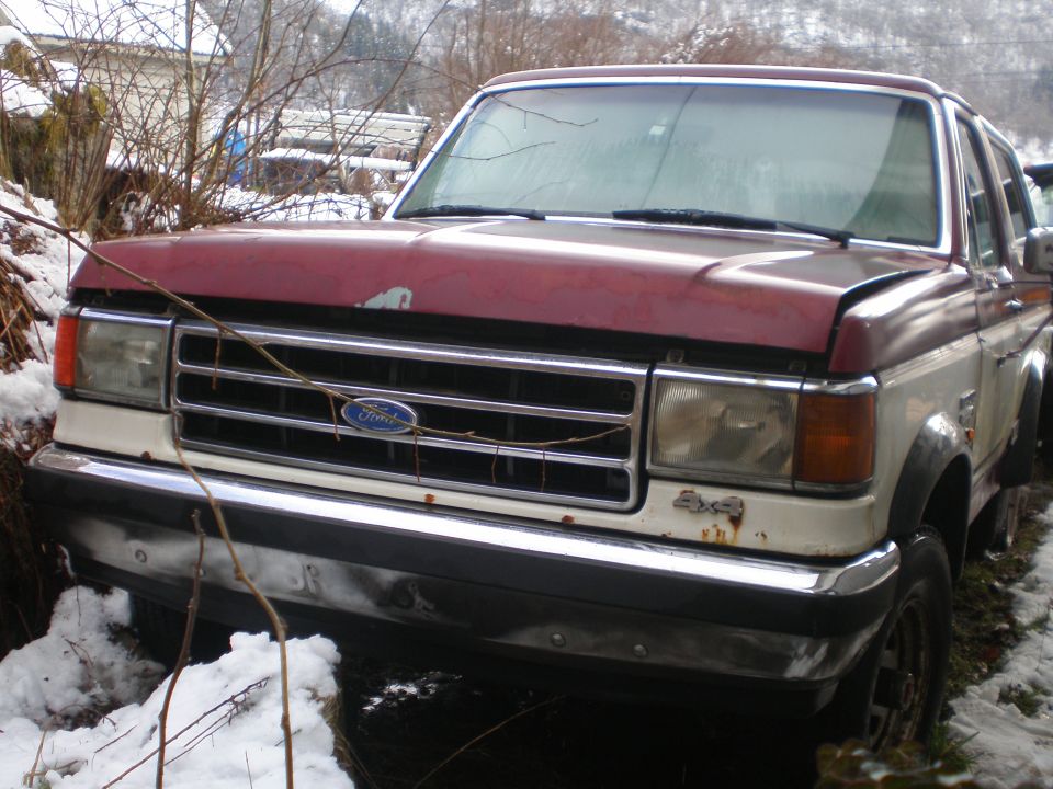 Maroon and white Ford Bronco with a chrome grille and 4x4 badge, parked in snow