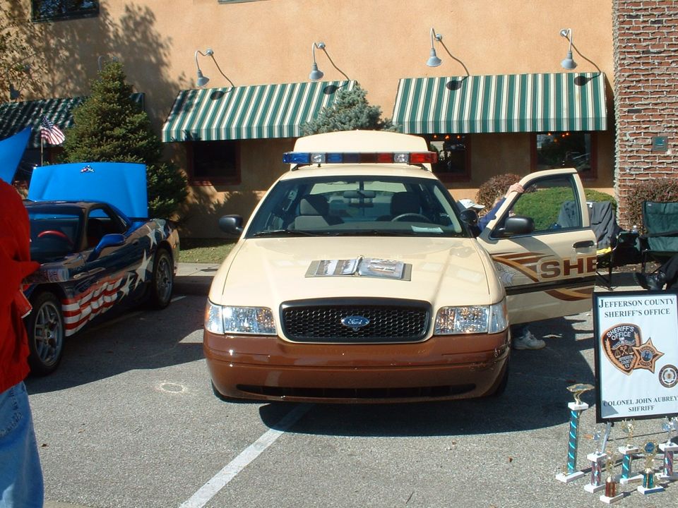Tan Ford Crown Victoria sheriff cruiser with roof light bar on display at a car show