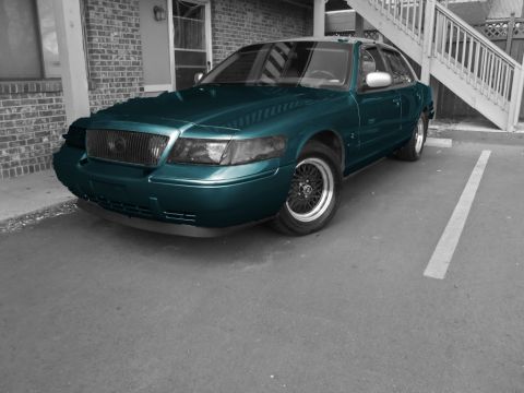 2000 Mercury Grand Marquis - A teal sedan is parked in a spot next to a brick building with an outdoor staircase.