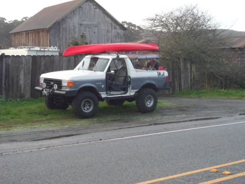 1991 Ford Bronco - Modified pickup truck with a kayak secured to the roof rack, parked near a rustic barn.