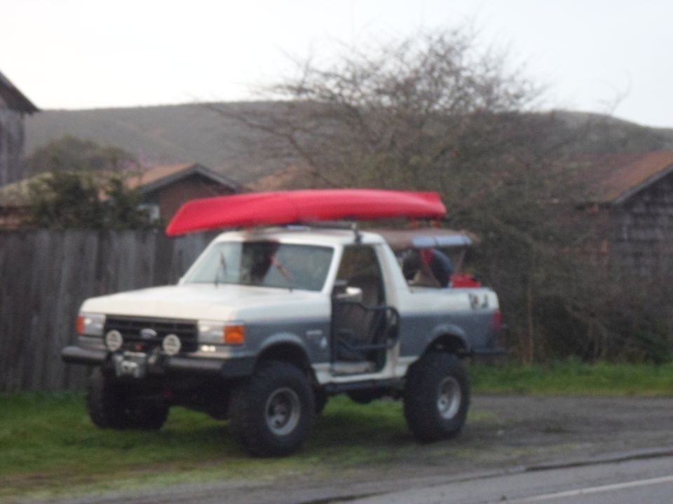 White and grey Ford Bronco with a red canoe on its roof rack