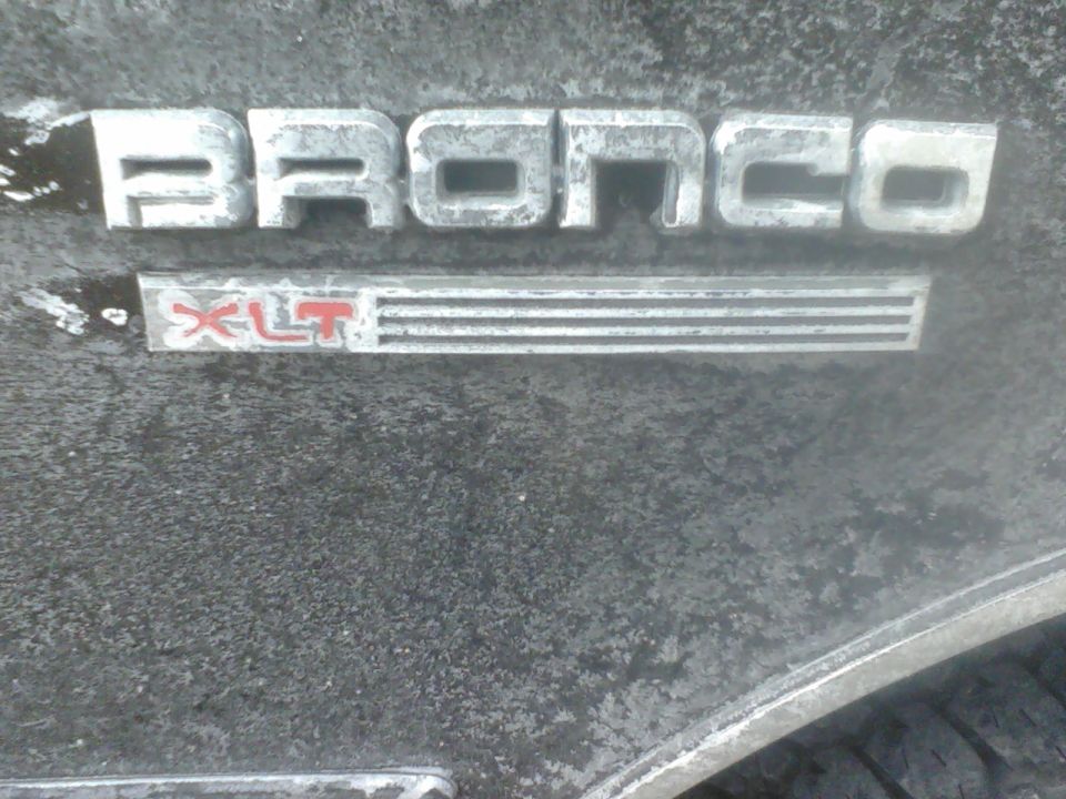 Bronco XLT emblem on a dark, weathered surface. Some dirt and water spots are visible