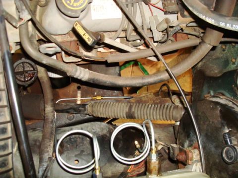 1995 Ford Bronco - The engine bay of a 1995 Ford Bronco shows various hoses, wiring, and a metal steering component with a rubber boot.
