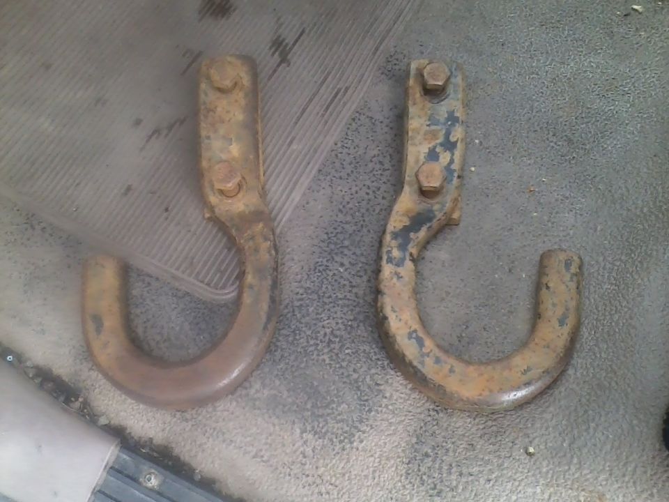 Two rusty tow hooks, one with black paint remnants, lying on a textured surface