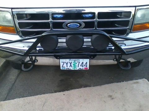 1992 Ford Bronco - Close-up of a Ford truck's front end, a chrome grille and a bull bar with auxiliary lights.