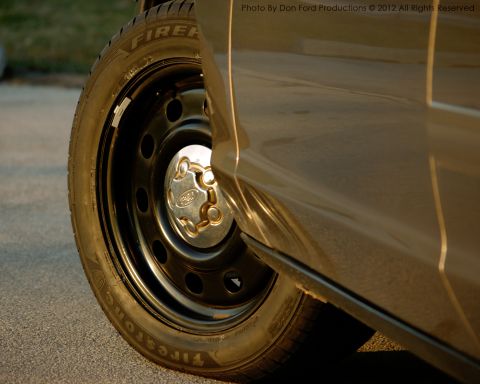 2005 Ford Crown Victoria - Close-up of the side of a 2005 Ford Crown Victoria, showing the wheel with a Firestone tire and a Ford-branded hubcap.